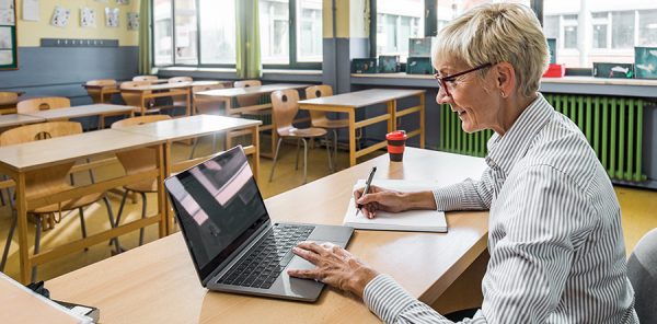 teacher in empty classroom teaching through laptop