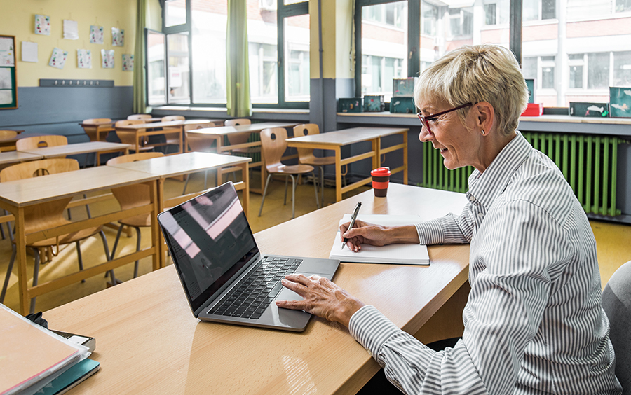 teacher in empty classroom teaching through laptop