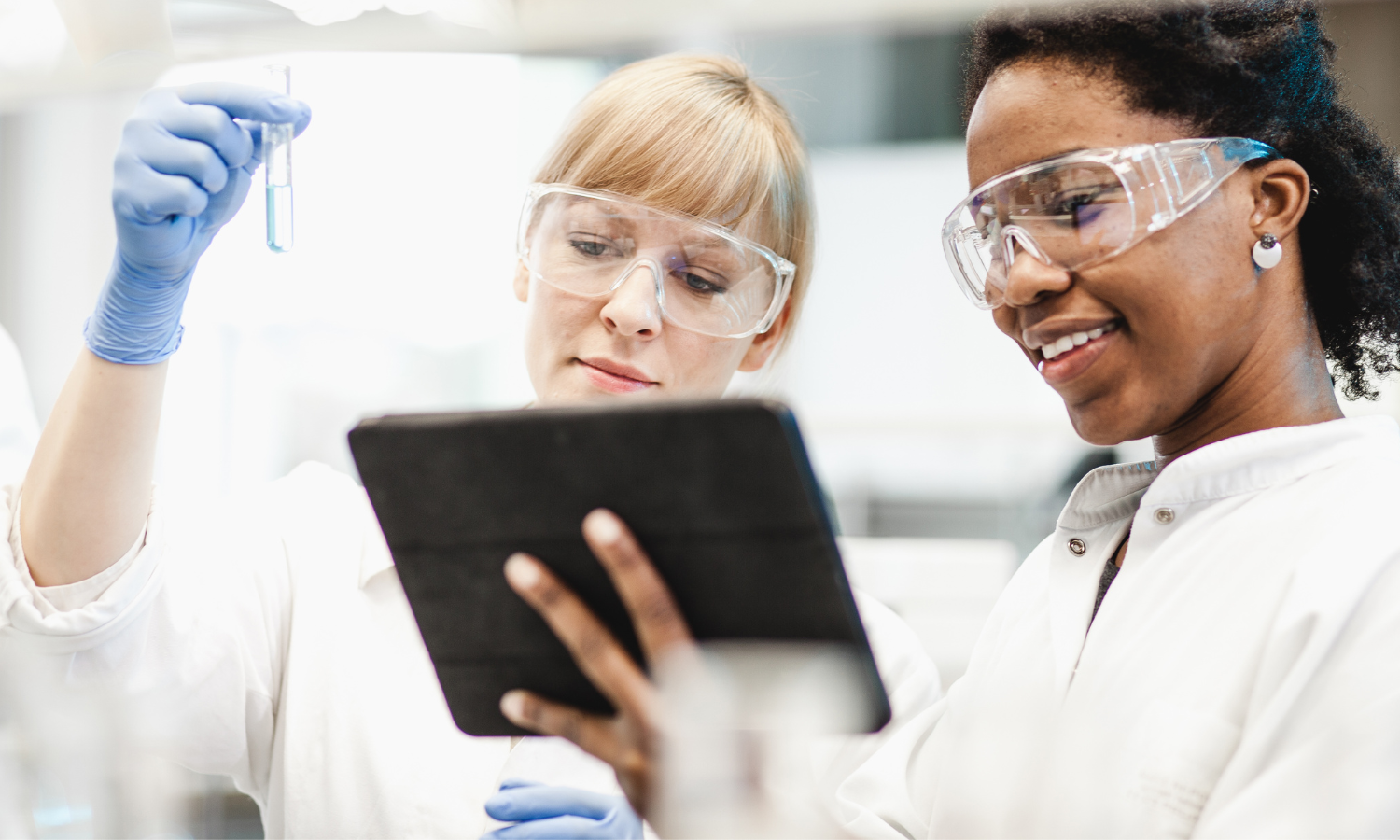 Two female scientists looking at a tablet and holding a vial