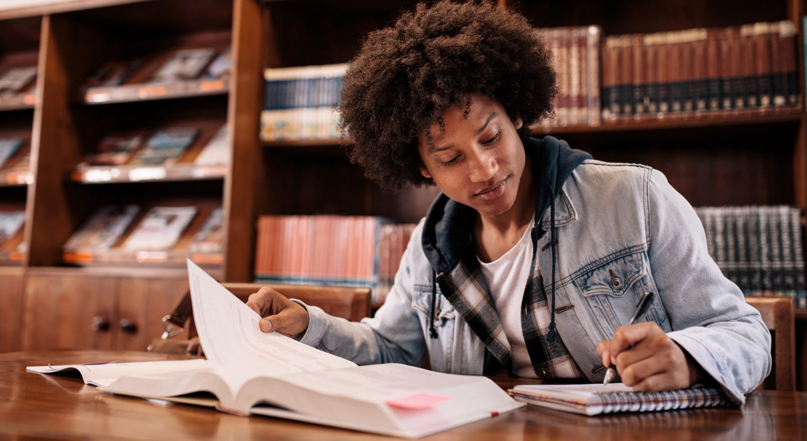 University student taking notes from book while sitting in the library.