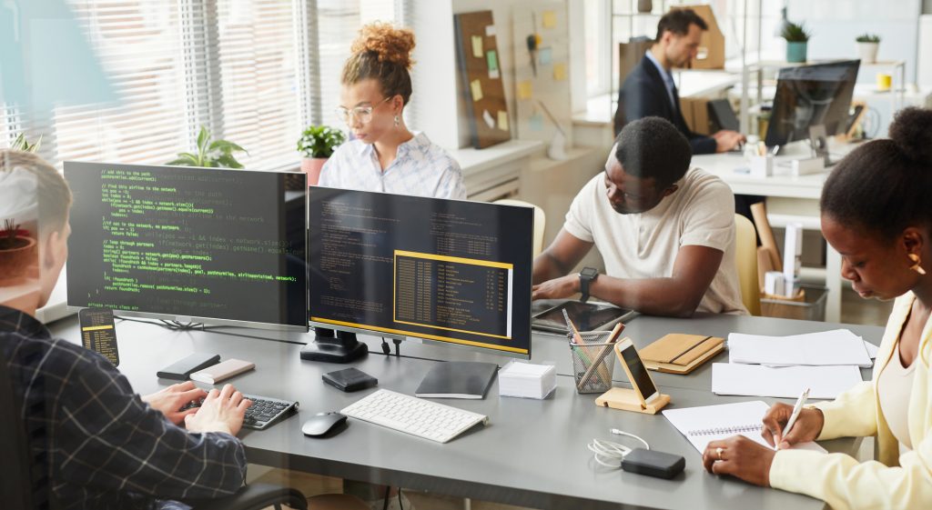 Group of programmers working in team with new project at table behind the window at office