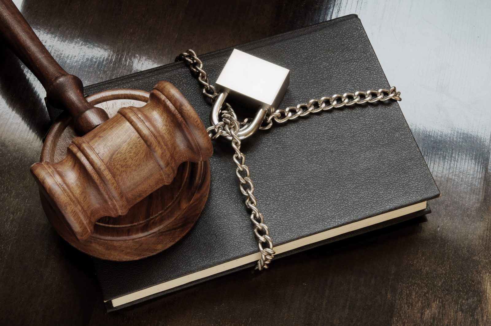 Book with wooden judge gavel, chain and padlock on wooden table