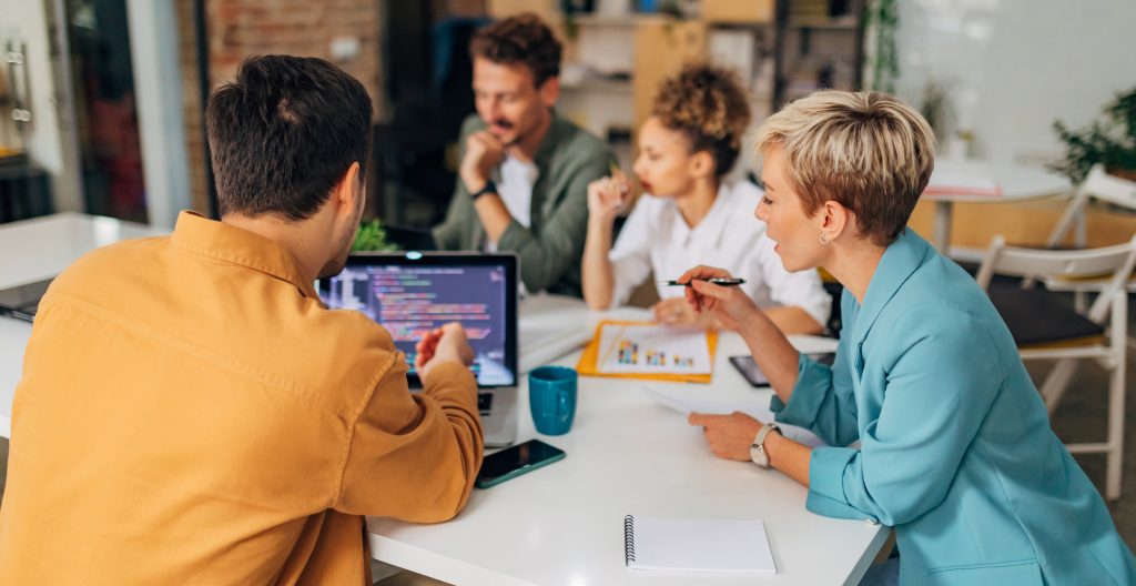 A male programmer shows a female colleague a coding technique while in business meeting.