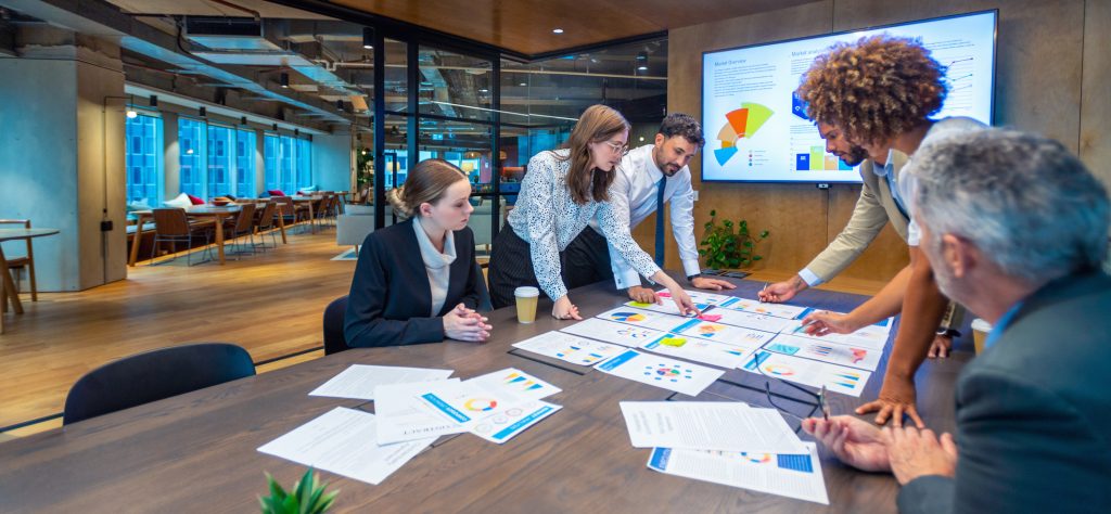 Paperwork and group of peoples hands on a board room table at a business presentation or seminar.