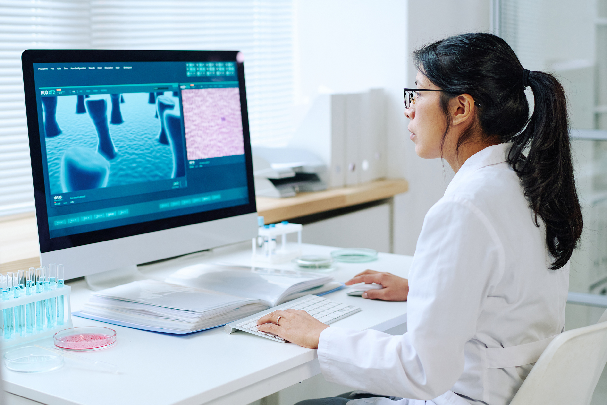 female virologist with dark long hair studying new virus while sitting by desk in front of computer in laboratory