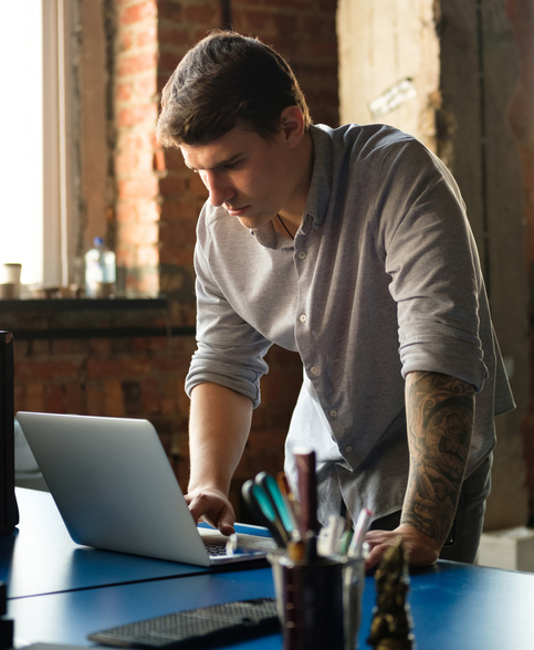 man leaning over table typing into laptop