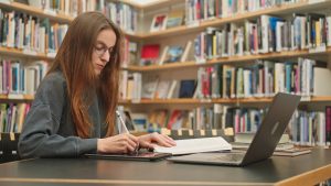 person doing research on computer in library taking notes