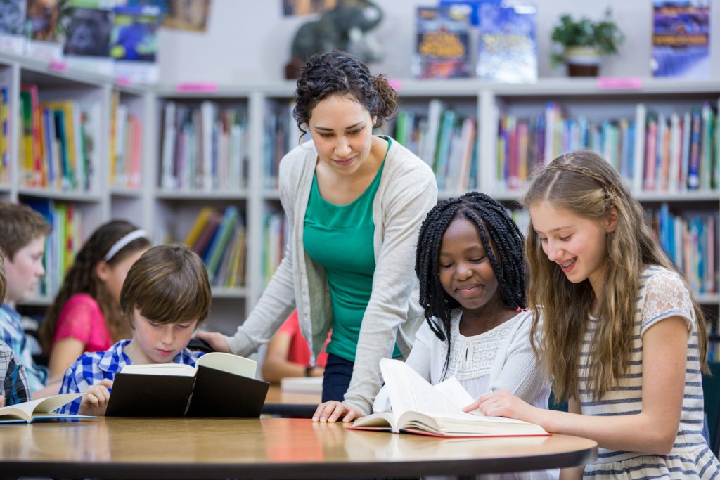 students reading books in classroom with teacher