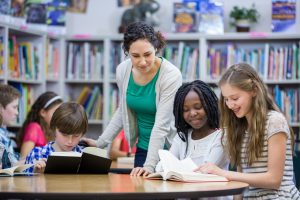 students reading books in classroom with teacher