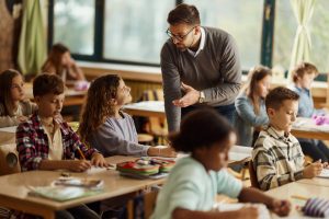 teacher helping student in classroom full of children